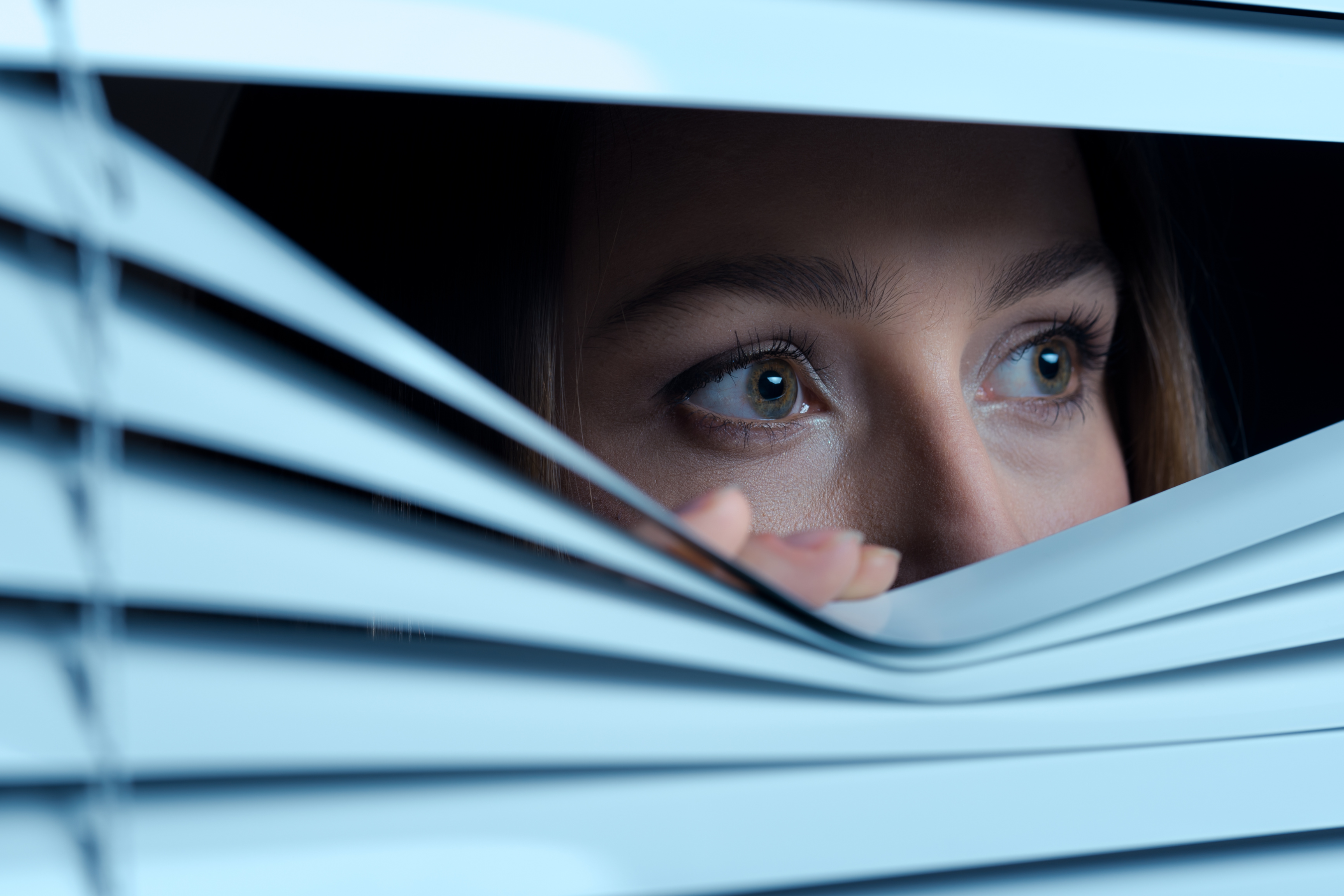 scared woman peeping from behind blinds
